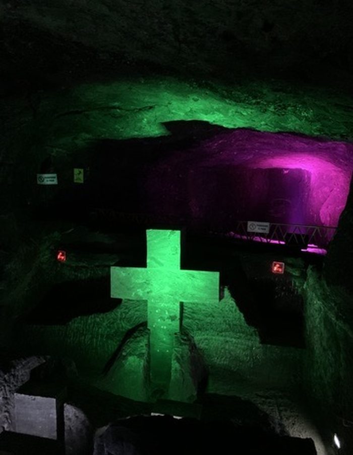Cruz tallada en sal iluminada en verde con fondo morado, en la Catedral de Sal